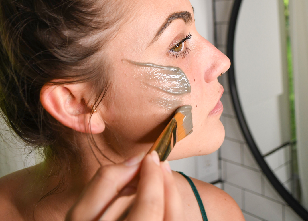 Woman brushing on facial mask in the mirror.