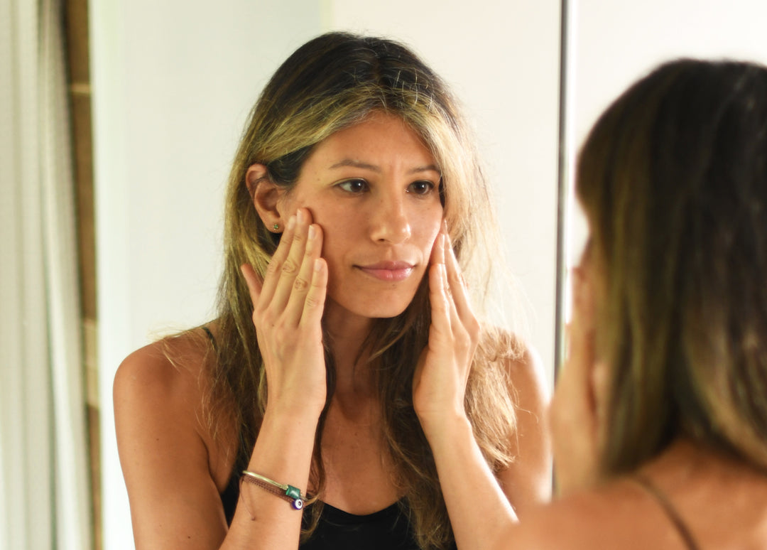 Woman looking at herself in the mirror rubbing oil on her face