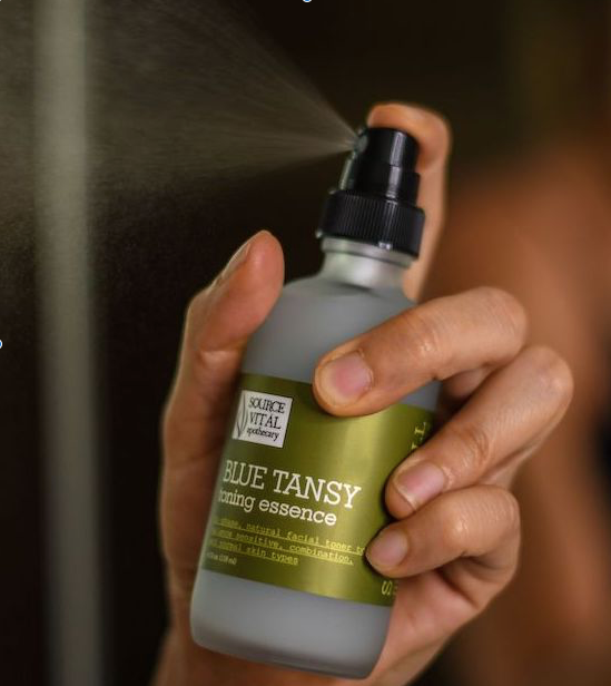 woman spraying toning essence on her skin with visible mist