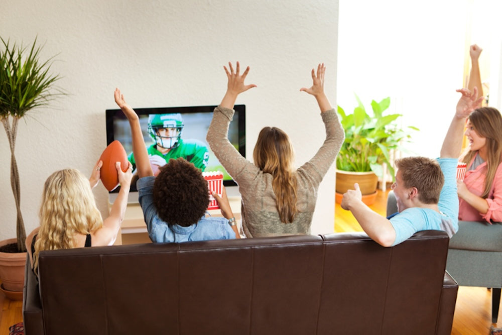 Group of people on couch watching football game while cheering