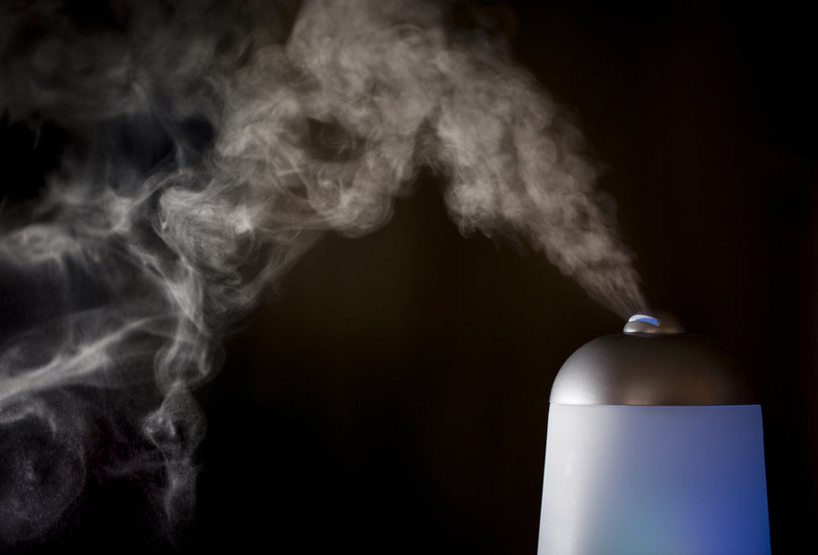 Silver and blue essential oil diffuser with mist coming out against black background