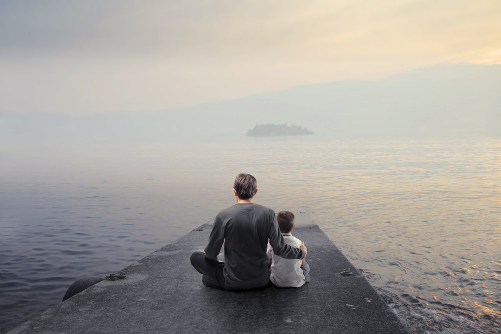 Father and son sitting on dock at sunrise over a foggy lake