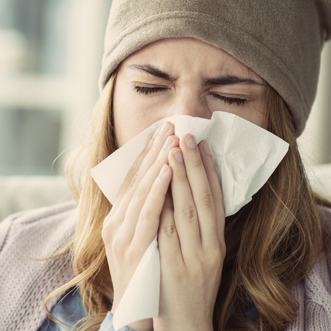 Woman blowing nose wrapped up in blanket sick