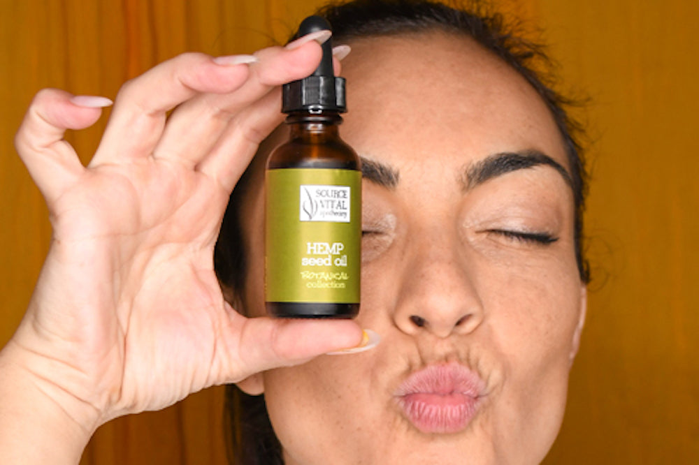 Woman holding bottle of hemp seed oil while closing her eyes and puckering her lips