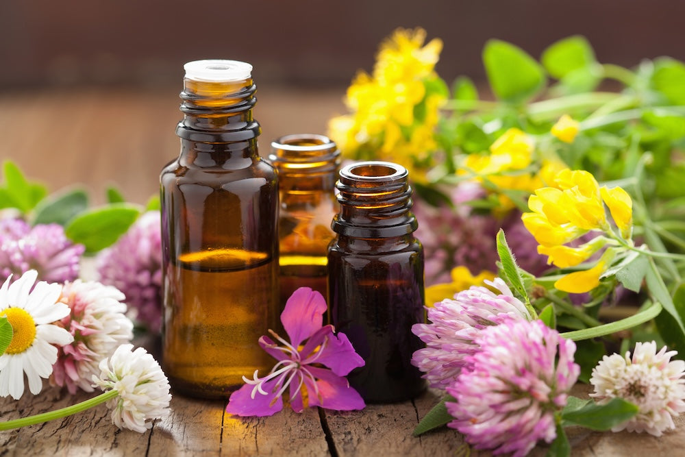 Glass amber essential oil bottles surrounded by various flowers