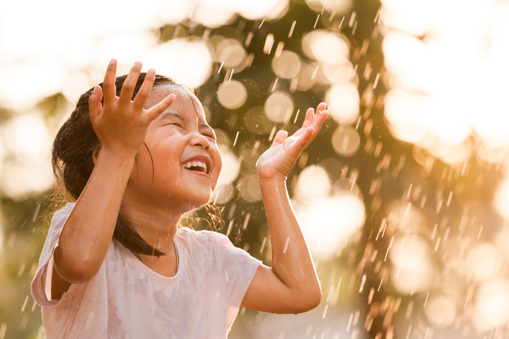 young girl with pigtails running through the rain, laughing