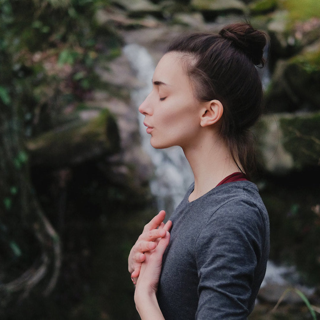 Woman with hands on chest deeply breathing against waterfall background