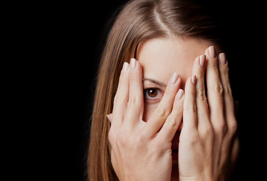 Brunette woman with sensitive skin hiding behind her hands with one eye visible