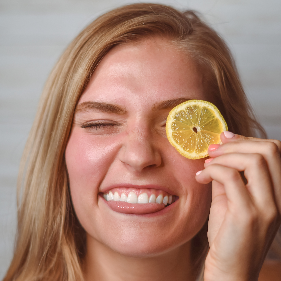 Blonde Lady Smiles with a Lemon Slice over her eye - summer skin care swaps by Source Vital Apothecary