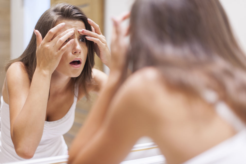 Woman looking in mirror with surprised look and fingers on her forehead, examining her acne