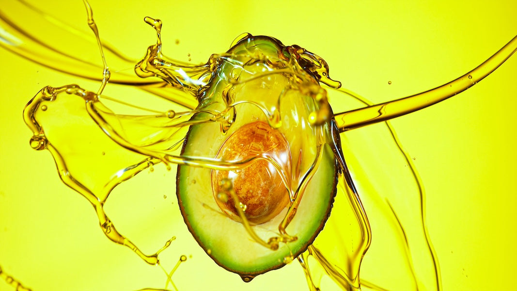 Avocado half being splashed with oil against green background