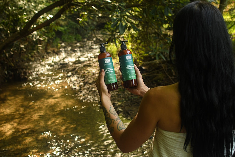 Woman holding Shampoo and Conditioner in the woods.