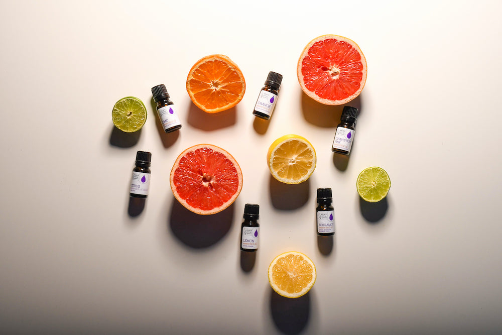 Various citrus fruits cut open surrounding source vital apothecary's essential oil bottles. 