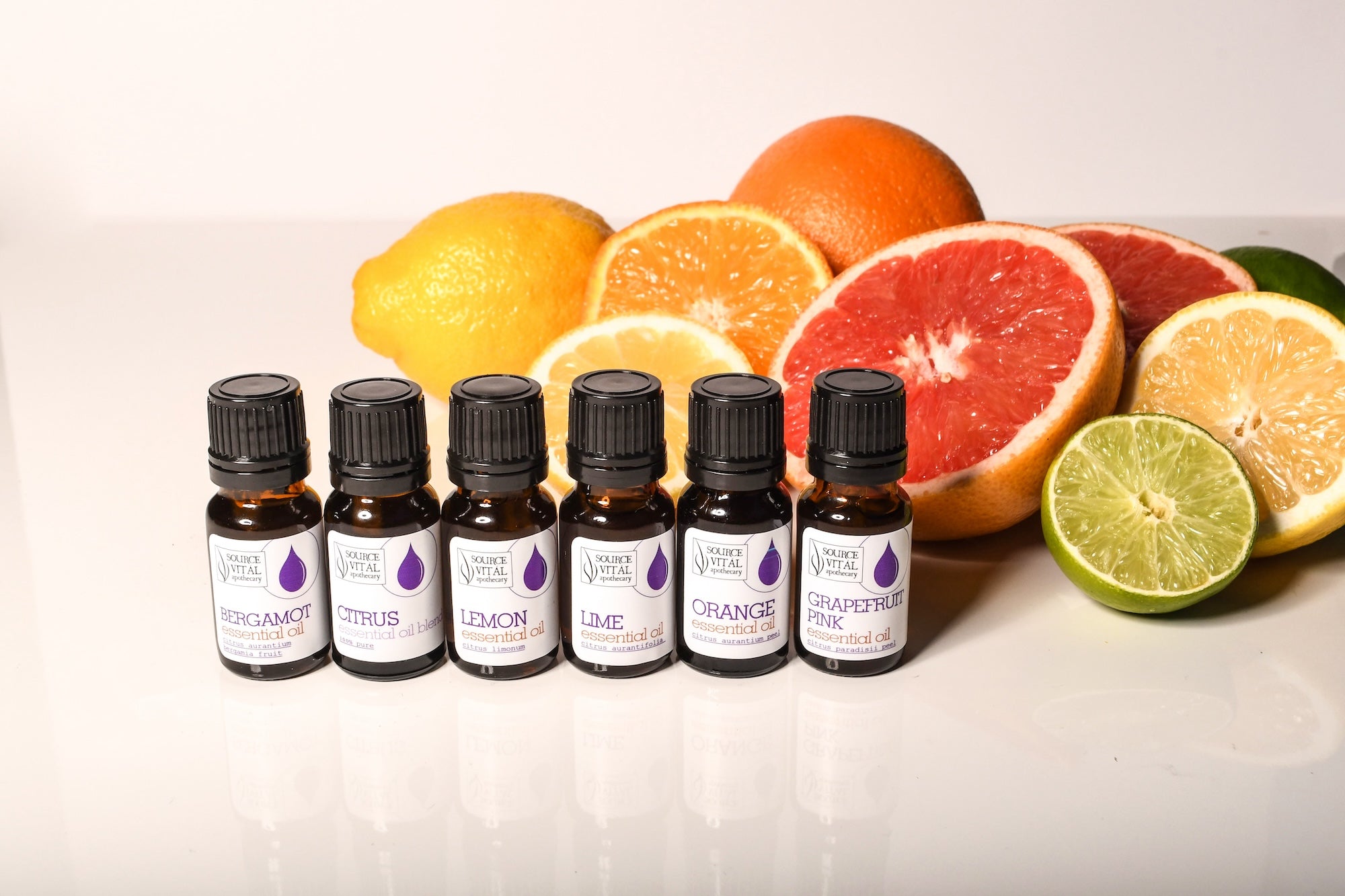 Citrus Essential Oils in a row with citrus fruits behind