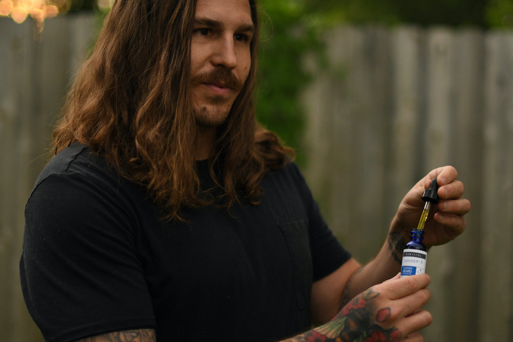 Man with full beard holding Sir Vital's Custom Beard Oil with dropper