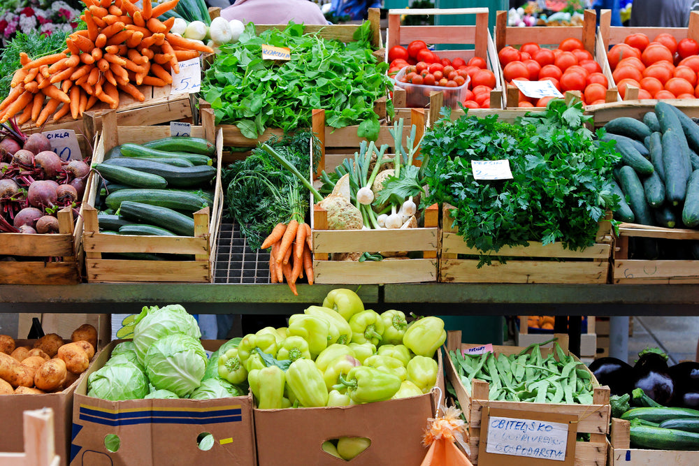 Farmer's market stand overflowing with numerous vegetables in wooden crates and cardboard boxes.