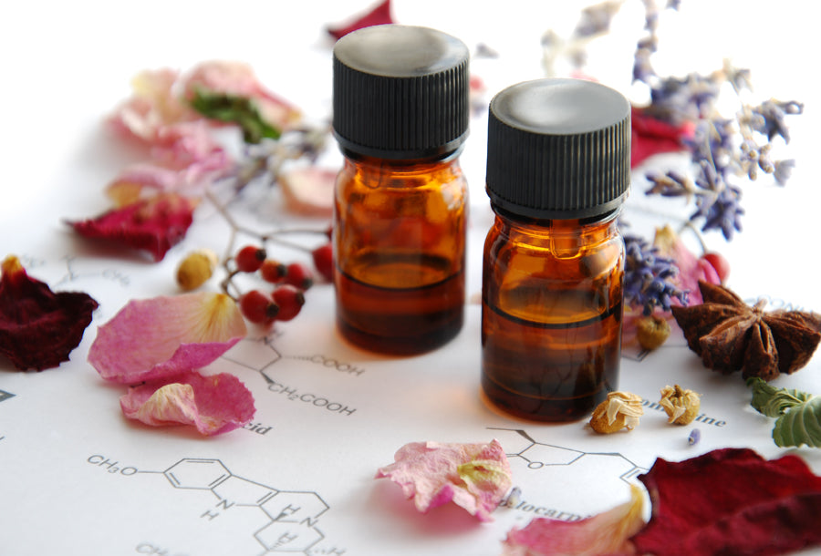 Two amber glass bottles full of essential oils surrounding by raw ingredients, such as flowers