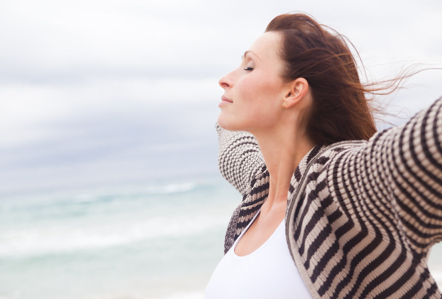 Woman at the ocean spreading arms wide and breathing deeply.
