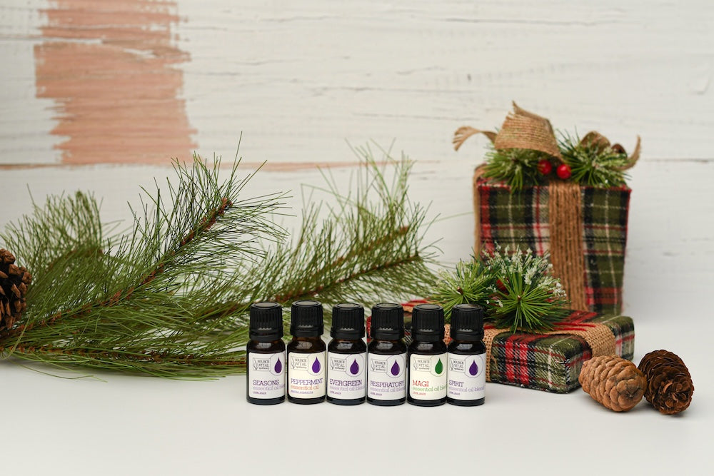 2023 Source Vital Holiday Scents Kit against evergreen bough and wrapped plaid packages.