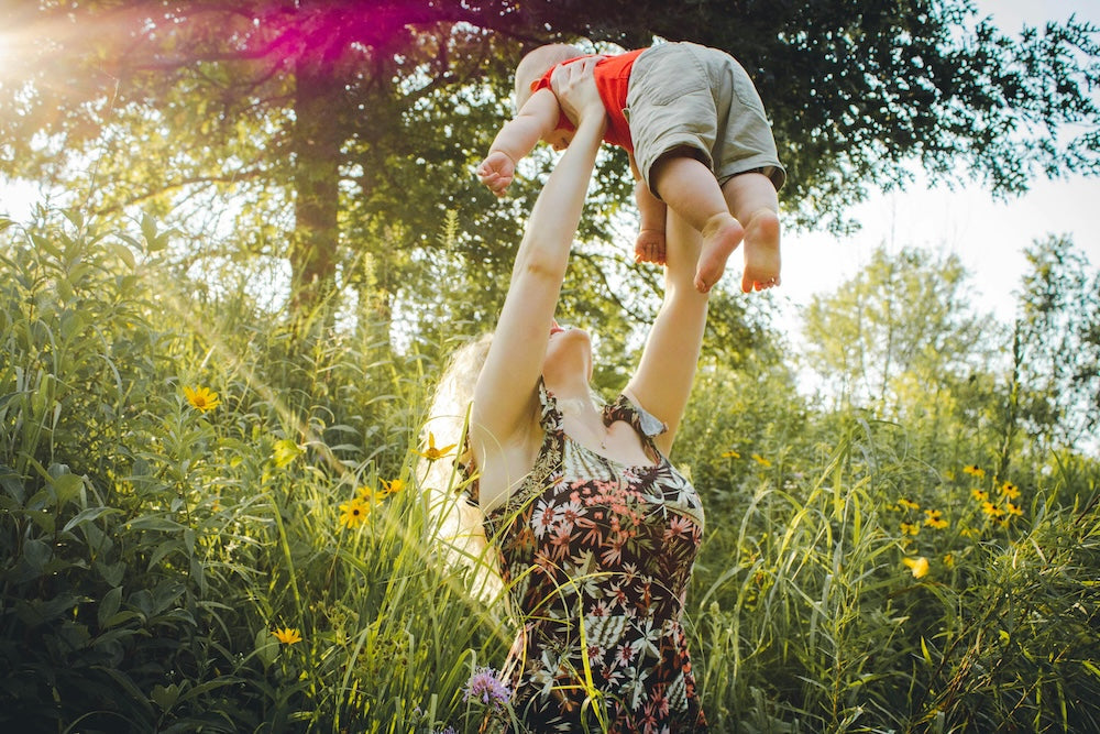 Woman holding child in the air surrounded by flowers and grass