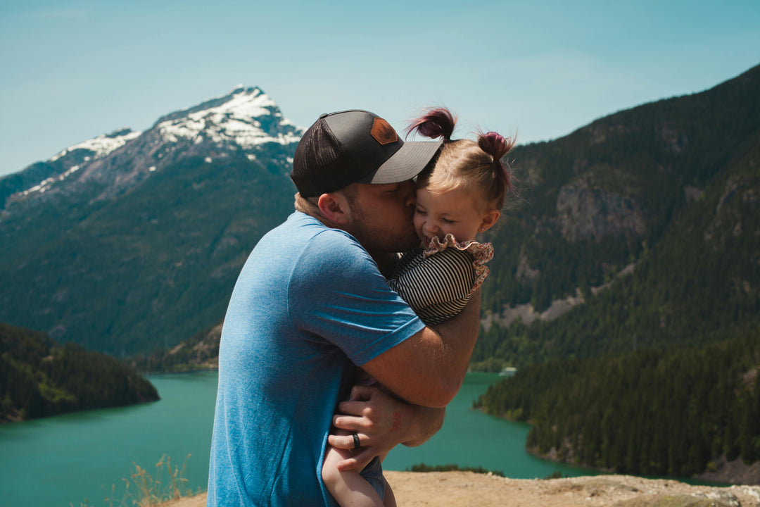 Man hugging daughter with mountains and lake in background.