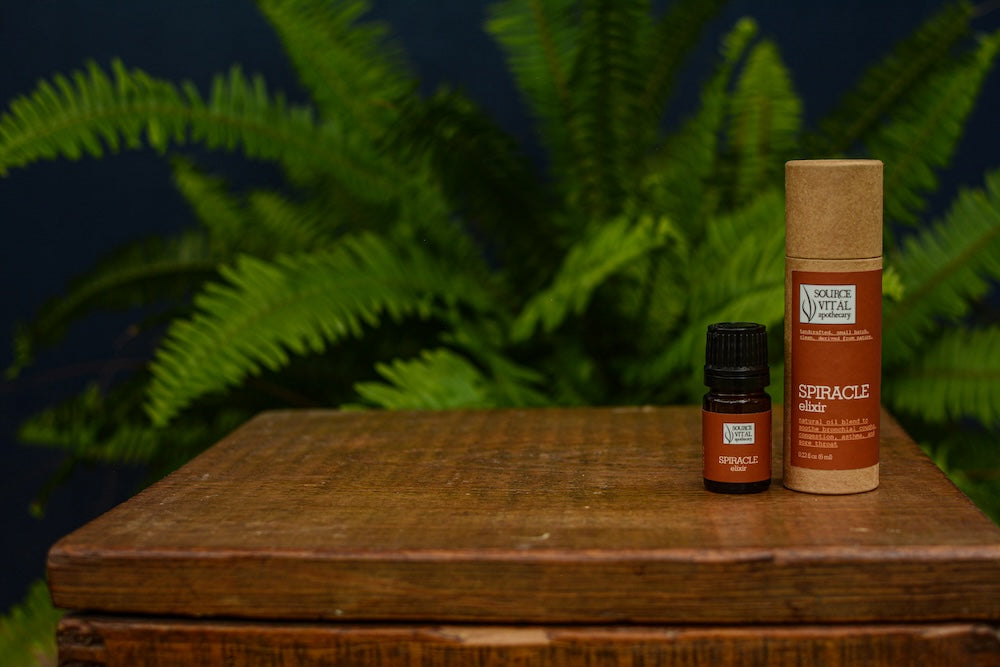 Spiracle Natural Elixir on wooden table against green fern background